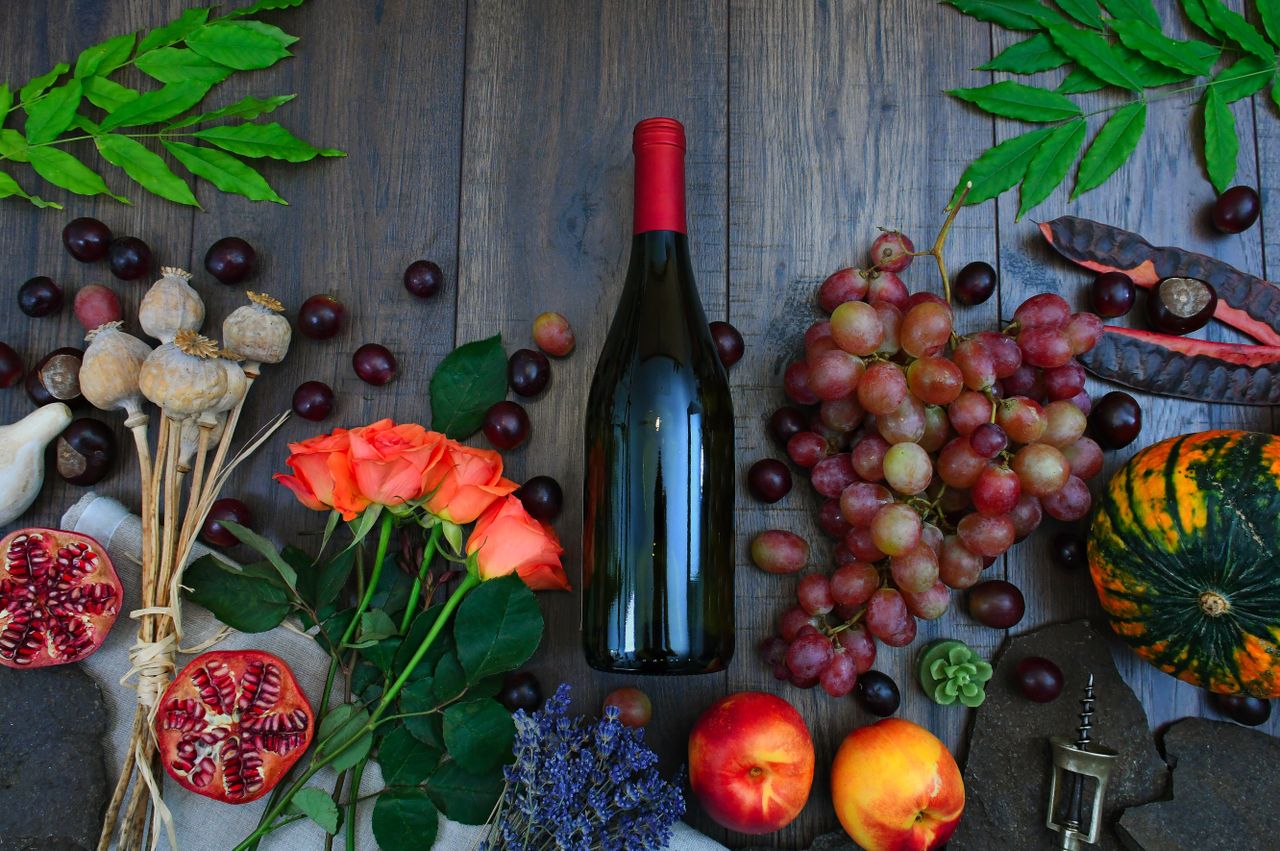 quality-assurance-02 A colorful display of autumn harvest with wine, fruits, and florals on a wooden table.