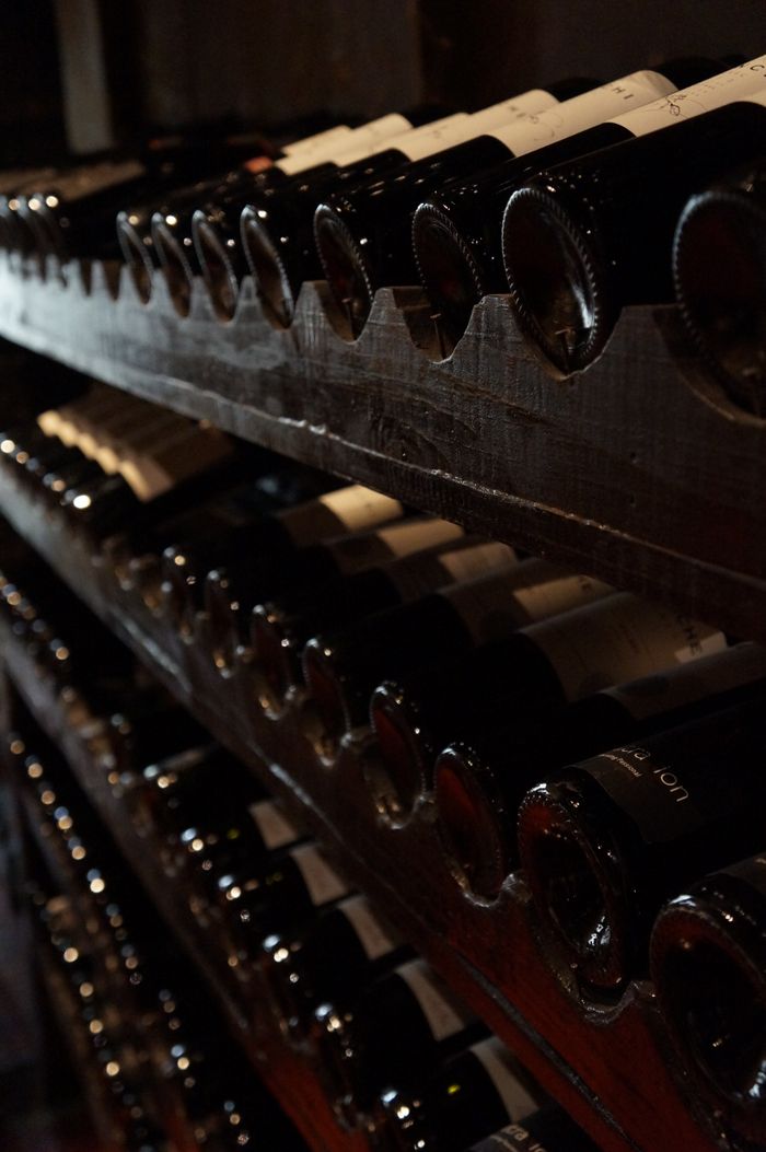 social-feed-img-03 A dimly lit wine cellar showcasing rows of wine bottles on rustic wooden shelves, creating a classic and elegant atmosphere.